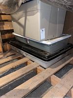 Three stacked plastic storage bins of various sizes and colors on wooden pallet.