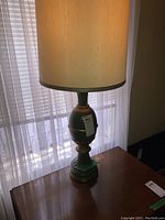 Full view of the table lamp on wooden surface near window, showing beige fabric shade and entire lamp base.
