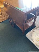 View of tea cart showing one fold-down leaf, large wooden wheel, and lower shelf.