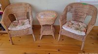 Full view of two wicker chairs with floral cushions and matching wicker side table between them on hardwood floor.