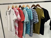 Seven men's t-shirts hanging on hangers displaying different colors and patterns including solid, striped, and textured styles.