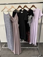 Five dresses hung on a rack including gray beaded evening dress, dusty pink sleeveless dress, black beaded dress, black casual dress, and pastel lavender casual dress
