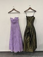 Front view of the purple beaded strapless maxi dress with thin clear straps and full skirt, alongside the dark green strapless maxi dress with satin finish and thin dark straps.