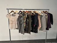 Photo of 11 women's tops and jackets hanging on a clothing rack showing various colors and styles from the 1990s.