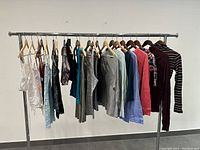 Photo showing multiple women's tops and t-shirts hanging on a rack, including sleeveless and long sleeve tops in various colors and styles.