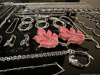 Close-up showing multiple silver tone chains, bracelets, earrings, and rings along with pink leaf earrings