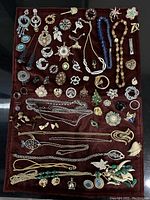 Photo showing an assortment of vintage brooches, chains, necklaces, and earrings arranged on fabric.