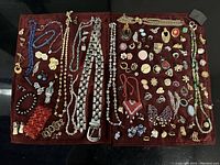 Overview of the lot showing a variety of vintage jewelry laid out on a dark fabric including necklaces, chains, earrings, and brooches.