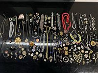 Overview of assorted vintage jewelry including brooches, chains, necklaces, and earrings laid out on a black surface