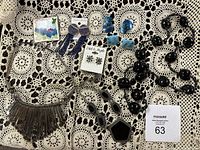 Overview of the lot showing a variety of vintage ladies' jewelry including a silver-tone bib necklace, black beaded necklace, and several pairs of earrings in blue, black and silver tones.