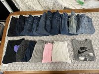 Photo showing multiple pairs of men's jeans and sweatpants laid out, plus gray Nike t-shirt with Air logo