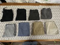 Eight pairs of men's pants and shorts laid on a patterned cloth showing color and style variety