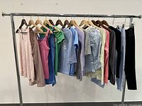Full view of the hanging clothing items from tank tops to long sleeve shirts and two pairs of pants on a clothing rack