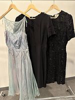 Three vintage dresses hanging side by side: light blue sheer beaded dress, plain black short-sleeve dress, and black beaded dress.