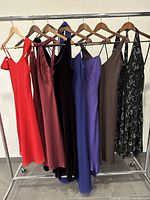 Six vintage dresses hanging on a rack showing variety of colors and styles including the Laura brand purple velvet dress from Chou Chou, made in France.
