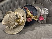 Side angle showing all three vintage designer hats stacked overlapping, displaying decorative fabric flower accents and woven materials.