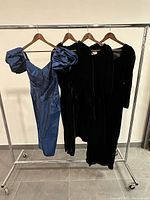 Four dresses on rack including three black velvet and one blue taffeta with puffed sleeves.