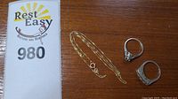 Chain and two rings displayed on wooden surface with auction sign
