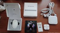 Wide view showing all items: Apple Mouse in box, USB SuperDrive box, Mac OS X Leopard DVD, Apple TV device with power cable, white EarPods in clear case