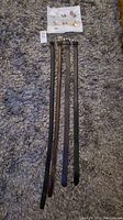 Four men's belts and assorted pins/buttons laid flat on carpet. Belts include two Perry Ellis and two other leather belts.