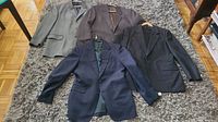 Four men's blazers and sports coats laid out on a carpet showing overall condition and color variety.