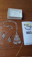 Top-down photo showing the necklace with a cascading pendant, two earrings, jewelry box, and Rest Easy tag number 983.
