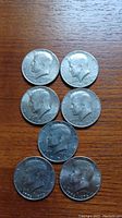 Seven Kennedy half dollar coins arranged on a wood surface showing the obverse profile of John F. Kennedy, dated between 1976 and 1978.