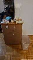 Photo of the wicker hamper with the hairdresser items and mirror placed on top, and the small plastic basket on the floor beside it.