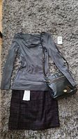 Photo of grey long sleeve top, plaid skirt, and small black handbag laid out on a carpet.