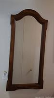 Full view of the wood framed mirror hanging on the wall, showing rectangular shape with arched top and medium brown finish.