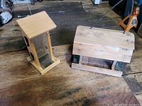 Two wooden bird feeders placed on a wooden floor, one vertical and one horizontal.