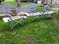 Three fold-up camp chairs arranged outside on grass showing side tables and cooler bags.