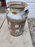 Side angled view of antique milk can showing rust and floral paint