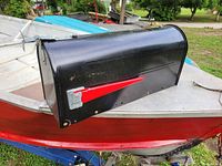Black metal mailbox with red flag showing side profile and overall condition.