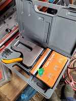 Open black plastic carrying case showing yellow handled cable stapler, box of assorted cable staples, and additional compartments.