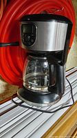 Front and side view of the coffee maker showing digital control panel, stainless steel body, and glass carafe.