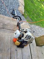 Side angled shot of the Echo trimmer showing the engine, fuel tank with orange cap, and pull start handle.