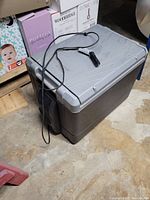 Closed electric cooler showing gray lid and dark gray body with power cord on top