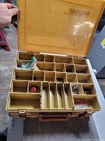 Top view of yellow fishing tackle box with lid open showing multiple compartments and some fishing accessories inside.