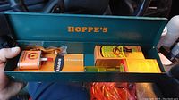 Metal green Hoppe's box opened showing contents including cleaning oil bottles and accessories