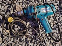 Full view of cordless electric hammer drill laying on gravel with attached power cord and side handle.
