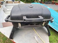 Closed portable camp BBQ grill with dome lid and thermometer on top, showing general exterior condition.