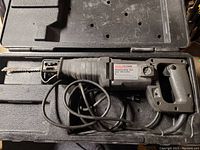 Top view of reciprocating saw inside carrying case, showing saw blade, handle, and power cord.