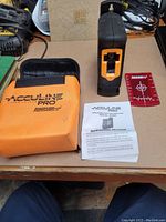 Front view of Johnson Acculine Pro laser level, orange soft carrying case, red target card, and instruction manual on a workbench.