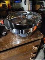 Stainless steel pot with lid sitting on a wooden surface in a storage area.