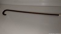 Full view of the wooden walking cane with curved handle, showing overall shape and length.