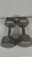 Pair of 25 pound hexagon cast iron dumbbells showing embossed weight '25' on sides, with visible wear and rust.
