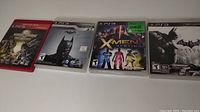 Four PS3 games laid out in a row showing front cover art for Mortal Kombat versus DC Universe, Batman Origins, X-Men Destiny, Batman Arkham City