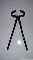Metal blacksmith tongs with rounded gripping head and long handles, shown from front view on a white background.