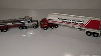 Side view of two toy oil tankers showing the Buddy L Texaco silver cylindrical tanker and the Canadian Tire larger white and red tanker with truck cabs attached.